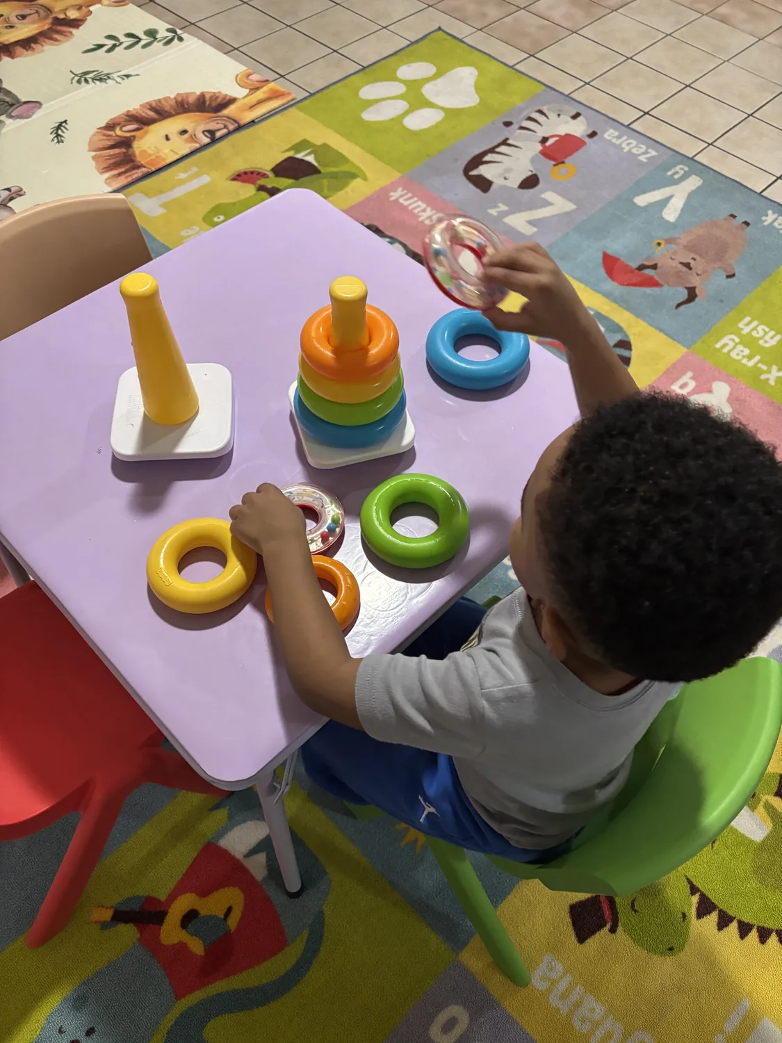 A young child practicing fine-motor skills with colorful stacking rings
